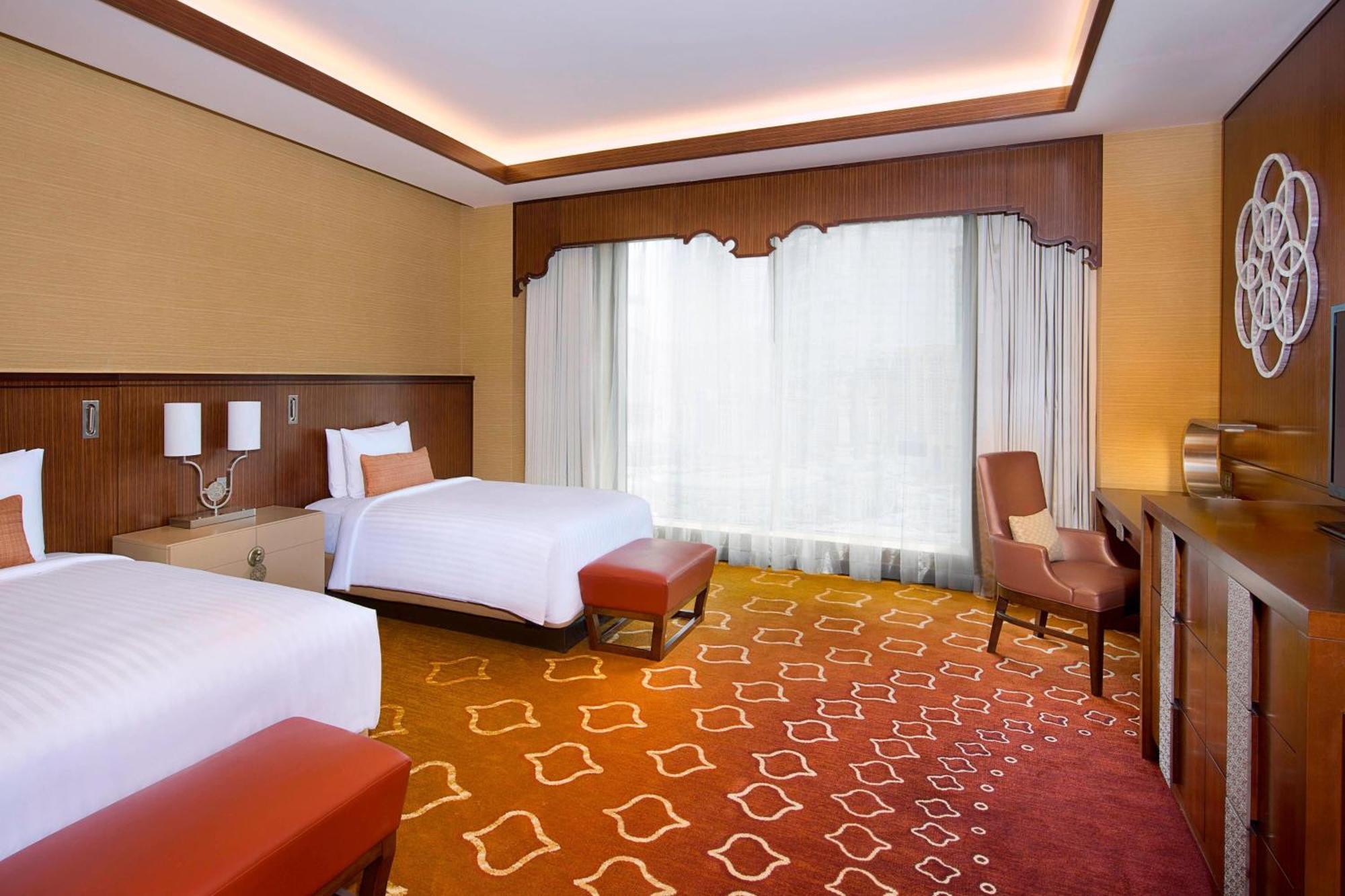 Jabal Omar Marriott Hotel Makkah Mecca Exterior photo The photo shows a well-appointed hotel room featuring two beds, one of which is a larger size. The room has a warm color palette with golden and orange tones, accentuated by a stylish carpet that has a geometric pattern. Large windows allow natural l