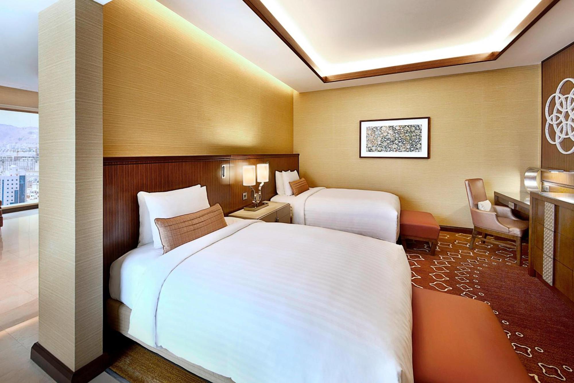 Jabal Omar Marriott Hotel Makkah Mecca Exterior photo The photo shows a modern hotel room featuring two beds with white linens. The room has a warm color palette, with beige walls and wooden accents. There's a piece of artwork on the wall above the beds. A small seating area is present, along with a wor