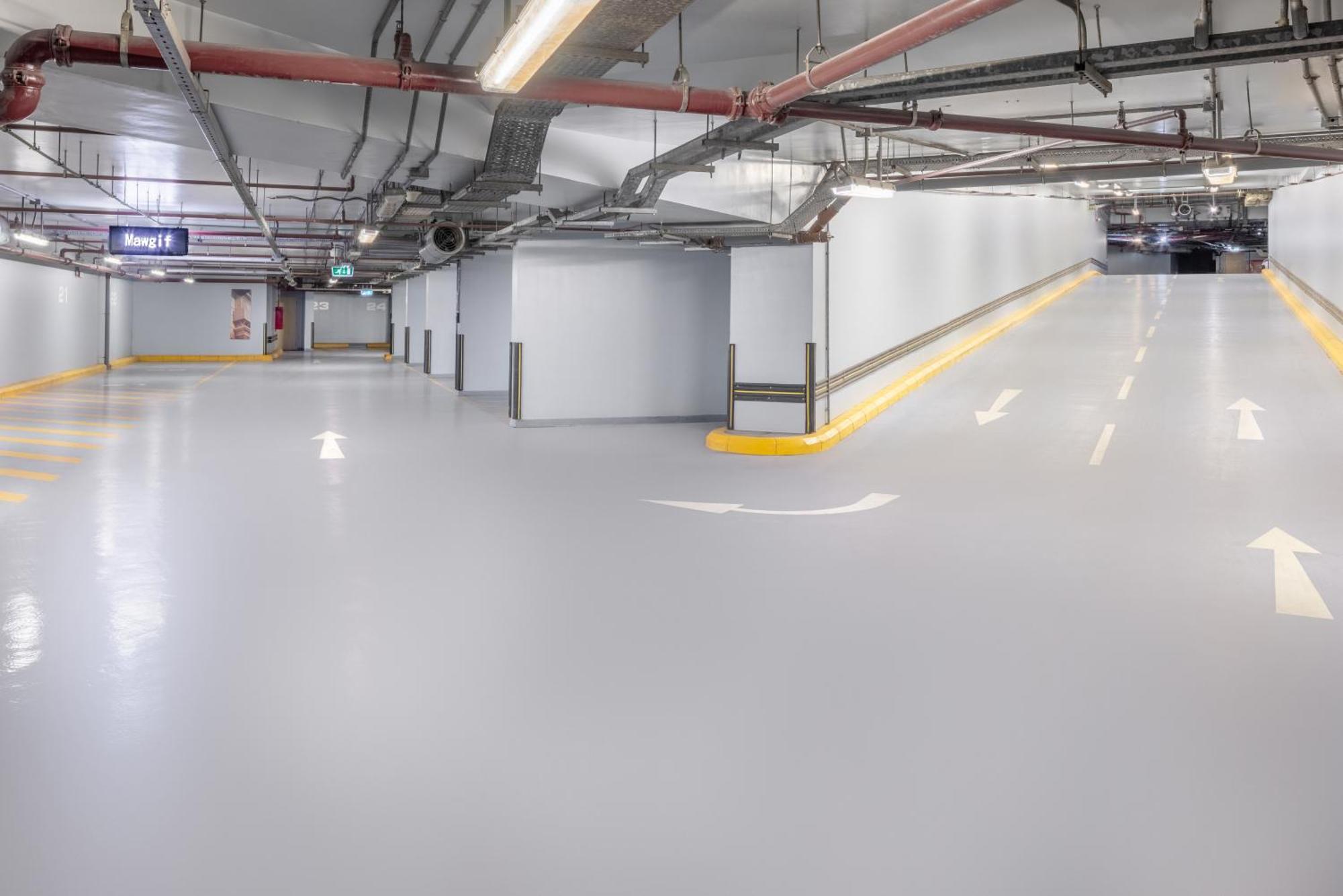 Jabal Omar Marriott Hotel Makkah Mecca Exterior photo The photo shows a spacious underground parking garage with smooth, light gray flooring. The walls are primarily white, and there are exposed pipes running along the ceiling. There are directional arrows painted on the ground, indicating the flow of t